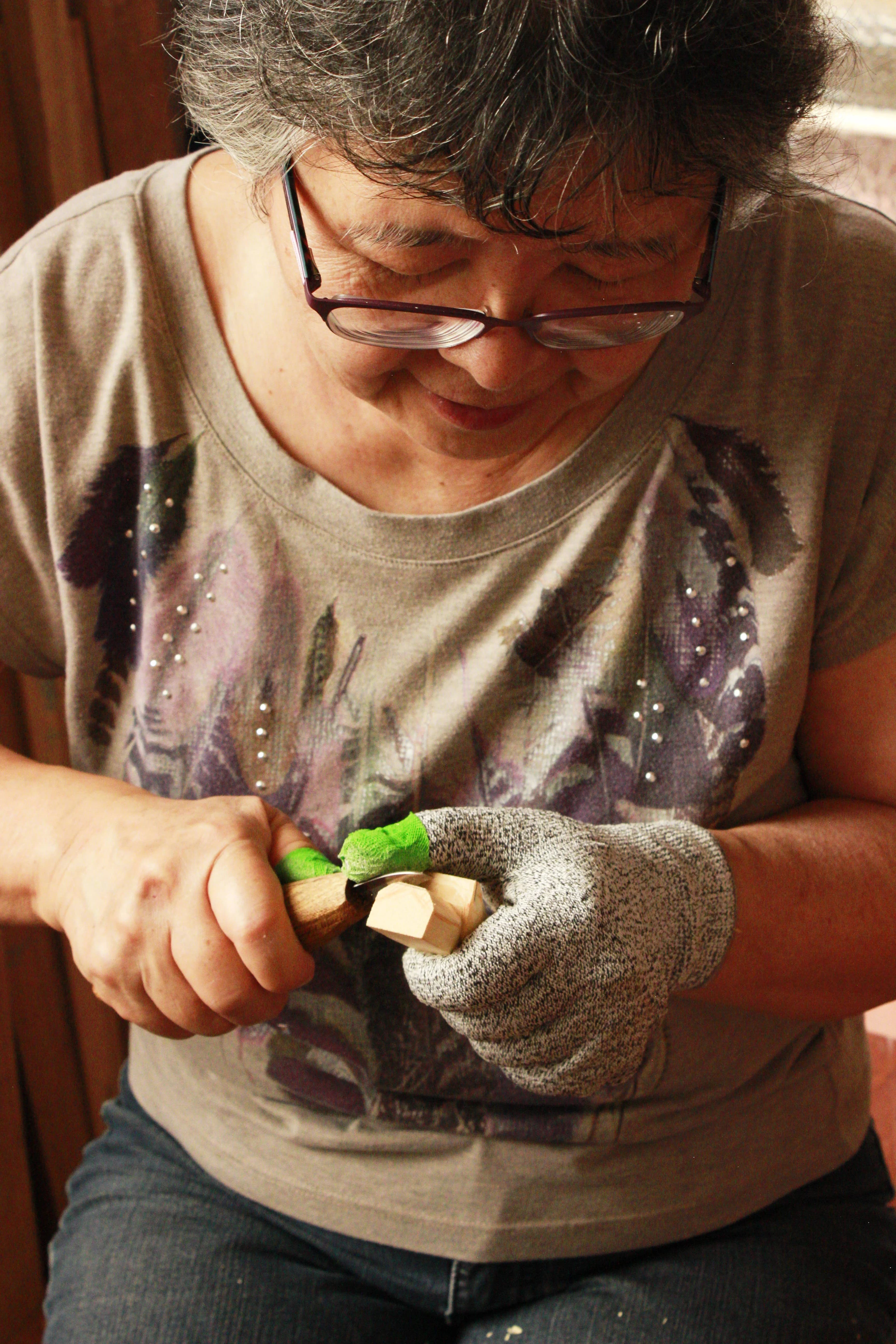 Mãe concentrada no entalhe à mesa, com ferramentas e madeira